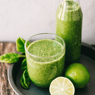 A glass and a bottle filled with green smoothie are placed on a tray with fresh spinach leaves and a whole and halved lime, highlighting the fasting benefits in every refreshing sip.