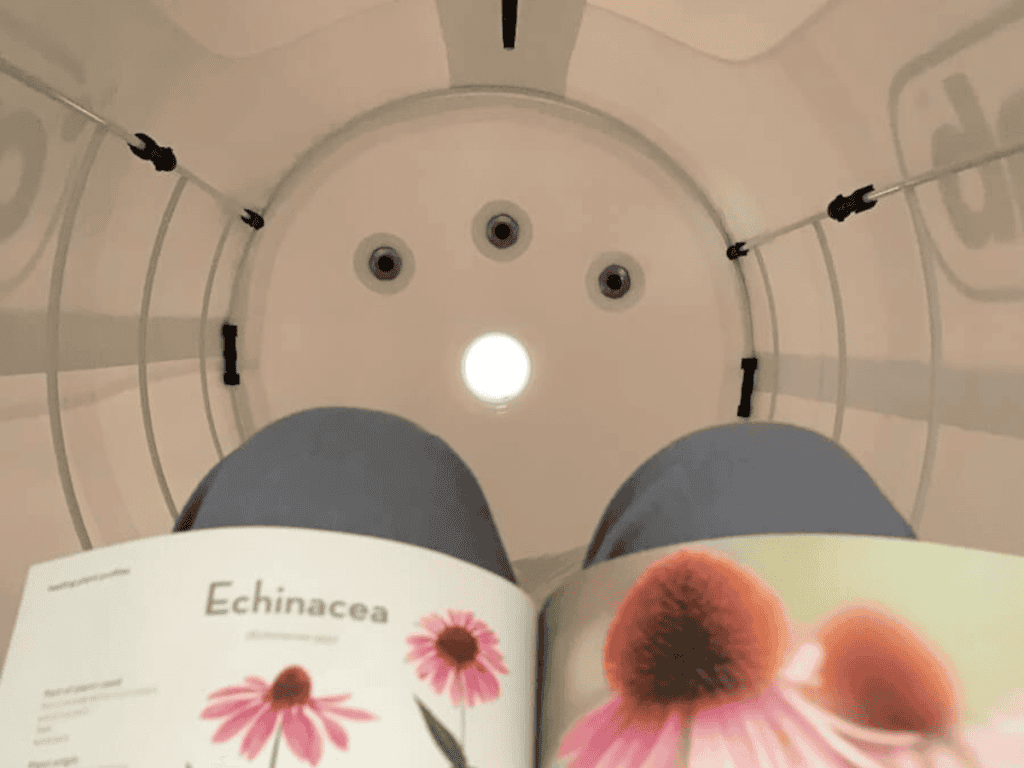 Person reading a book about Echinacea while sitting inside a cylindrical chamber with a light overhead.